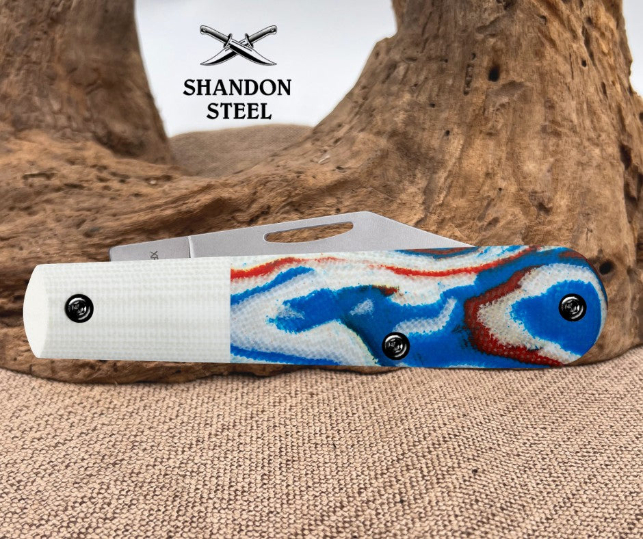Folding knife with colorful handle design on a textured surface, Shandon Steel brand visible
