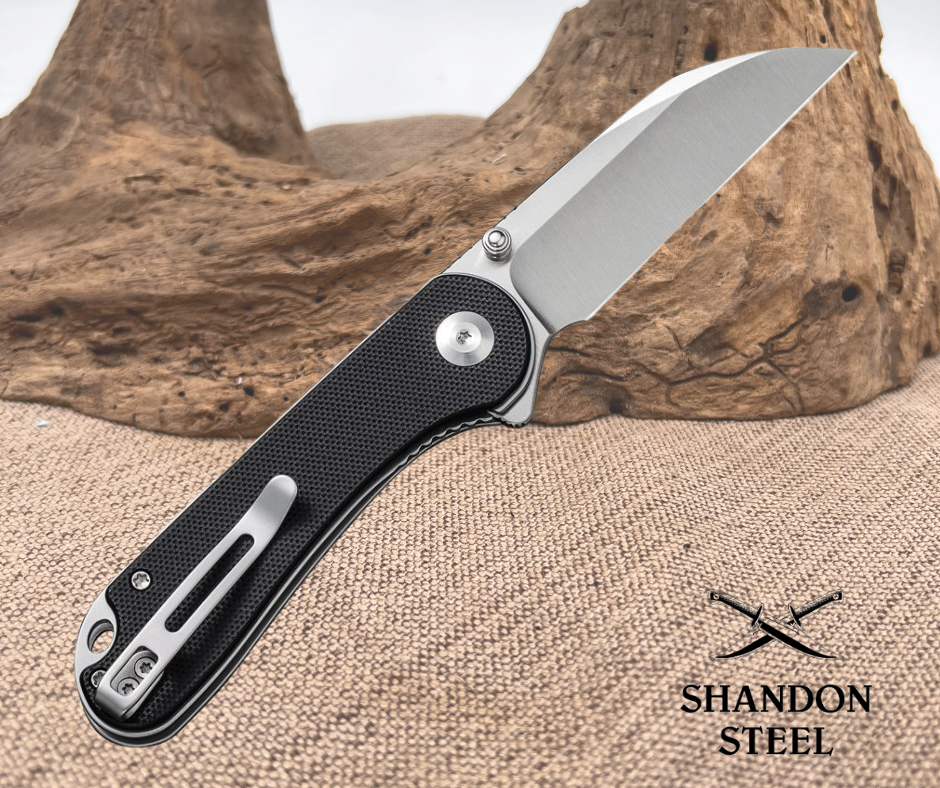 Folding knife with black handle and silver blade on a wooden background, Shandon Steel logo visible.