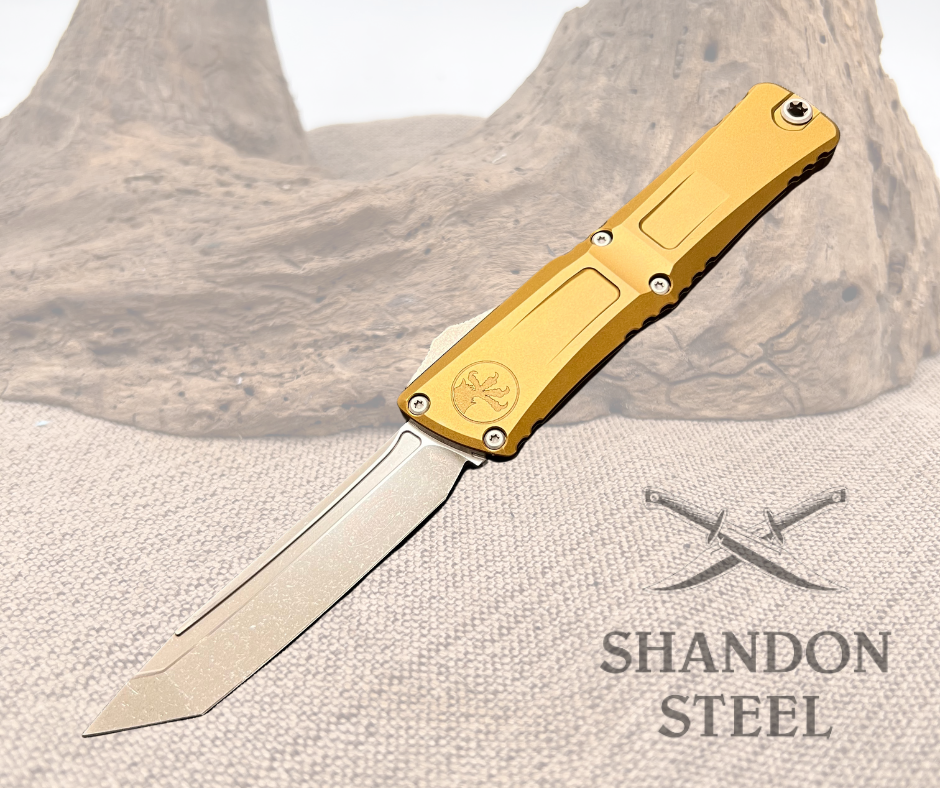 A gold-handled Microtech Combat Troodon knife with an apocalyptic blade, displayed open on a textured surface.