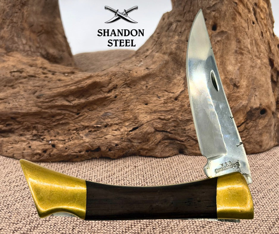 A folding pocket knife with a polished silver steel blade and a handle made of dark wood and brass, displayed against a rustic wood background. The brand name 'Shandon Steel' is visible at the top of the image.
