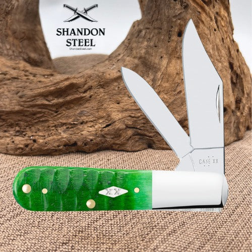 A folding pocket knife with a bright green and white handle, displayed open against a rustic wood background. The brand logo 'SHANDON STEEL' is visible in the upper left, and the knife is set on a burlap surface.
