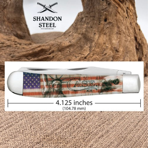 A folding pocket knife shown on a white background with a wood-and-burlap backdrop. The knife has a printed American flag design with Statue of Liberty imagery and the text 'CASE 22'.