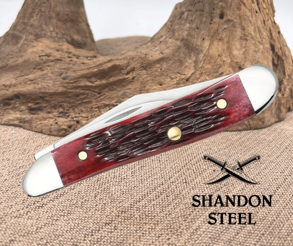 Knife with red handle and silver blade on a textured surface with 'Shandon Steel' branding.