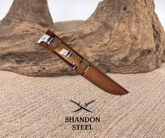 A brown leather belt sheath for a knife, displayed on a textured background, with the logo 'Shandon Steel' visible.
