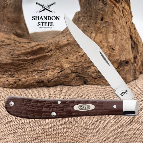 A folding pocket knife with a silver stainless steel blade and a dark brown textured handle, displayed on a burlap surface with a piece of driftwood in the background. The brand logo 'SHANDON STEEL' is visible in the upper left, and the 'CASE' logo is on the handle.