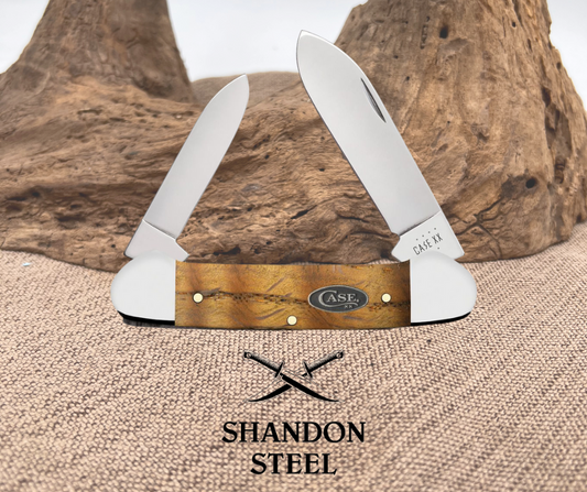 A Case XX folding knife with a yellow curly oak handle and stainless steel blades, displayed against a natural background.