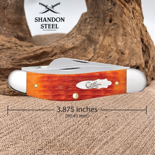 A folding pocket knife with a reddish-orange wood handle and silver metal blades, shown on a burlap surface with a piece of driftwood behind it. The image includes the Shandon Steel logo at the top and a dimension line indicating the knife is 3.