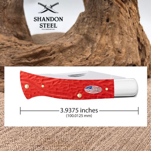 A red textured pocket knife shown on a white measurement card with printed text indicating 3.9375 inches and the brand name Shandon Steel at the top, set against a rustic wood and burlap background.
