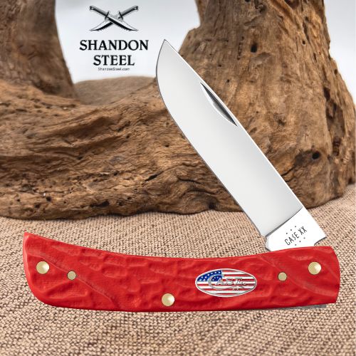 A folding pocket knife with a silver blade and a textured red handle, displayed on a burlap surface with a piece of driftwood and a white background card showing the 'Shandon Steel' logo.