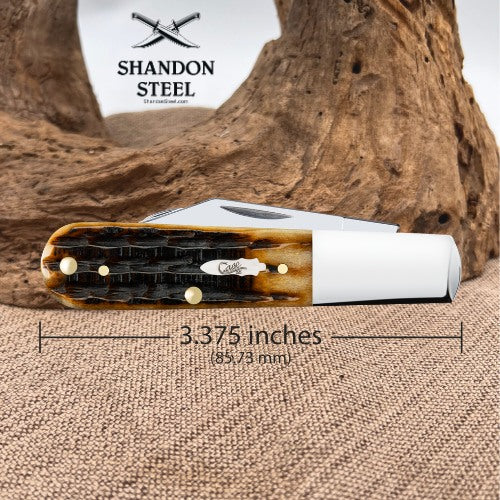 A folding pocket knife with a white handle and a brown-and-black patterned inlay, shown on a burlap surface with a piece of driftwood behind it. The Shandon Steel logo appears in the upper left, and a dimension line across the knife reads 3.