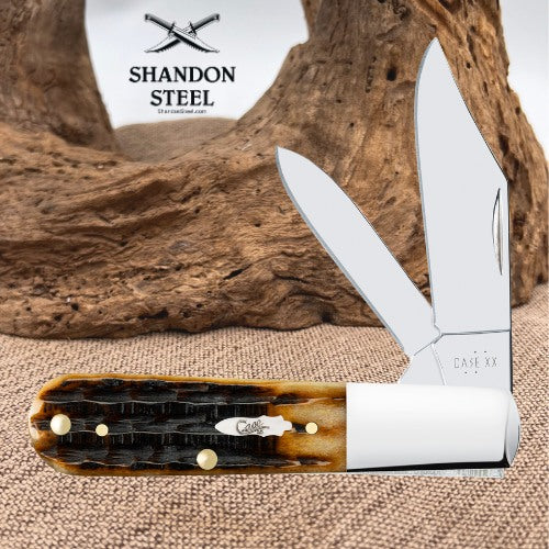 A folding pocket knife with a tortoiseshell handle and silver blades, displayed on a burlap surface with a piece of driftwood and a white Shandon Steel logo sign in the background.