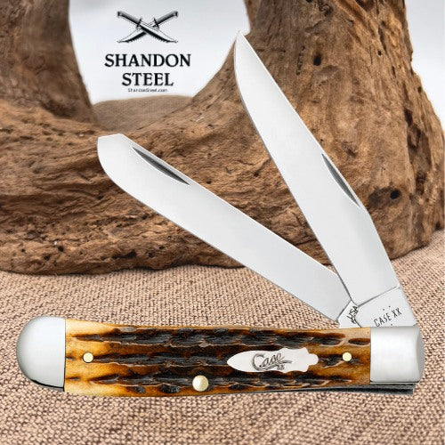 A folding pocket knife with a brown and black marbled horn handle and silver steel blades, displayed on a burlap surface with a piece of driftwood and a white Shandon Steel logo card in the background.
