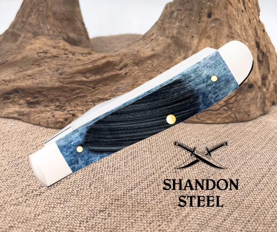 Folding knife with blue handle and white accents on a textured surface, Shandon Steel branding visible.