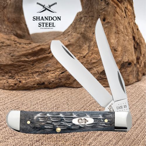 A double-blade folding pocket knife with a textured black and gray handle, shown open against a rustic wood driftwood background on burlap. The brand logo 'SHANDON STEEL' is visible in the upper left, and 'CASE 44' is stamped on the bolster.