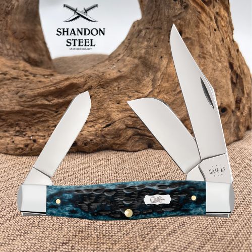 Shandon Steel Casey XX folding pocket knife with a blue marbled steel handle, shown with both blades open against a rustic wood and burlap background.