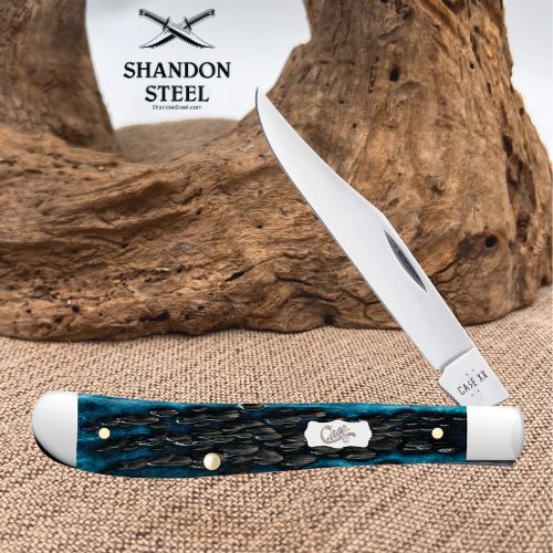A folding pocket knife with a silver blade and a textured blue-green handle, displayed on a burlap surface with a piece of driftwood in the background. The brand logo 'Shandon Steel' is visible in the upper left.