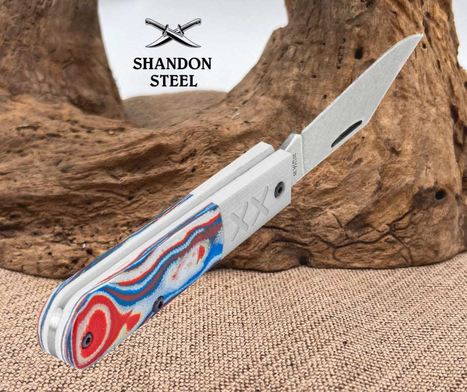 Folding knife with a colorful handle on a textured surface, featuring the Shandon Steel logo.