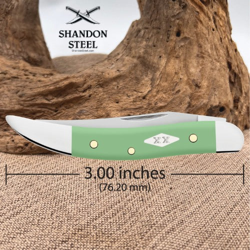 A green and silver folding pocket knife with dimension markings showing a 3.00-inch blade length, set against a rustic wood and burlap background with the Shandon Steel logo.