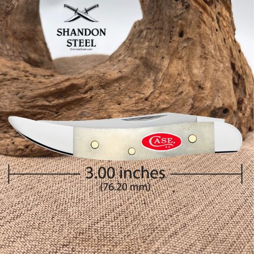 A folding pocket knife shown horizontally on a burlap surface with a piece of driftwood behind it. The knife has a silver blade, a light beige handle, and a red oval CASE logo.