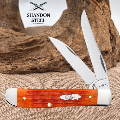 A double-blade pocket knife with a reddish-orange and white horn handle, shown open against a rustic wood and burlap backdrop. The brand logo 'SHANDON STEEL' appears in the upper left, and 'CASE XX' is engraved on the metal bolster.