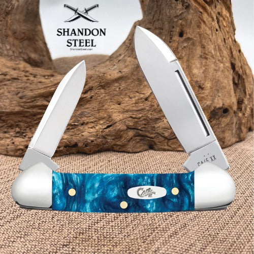 A folding pocket knife with a blue marbled resin handle and silver stainless steel blades, displayed against a rustic wood background with a white card reading SHANDON STEEL.