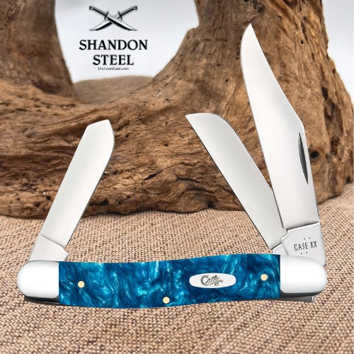 A folding pocket knife with a blue marbled handle and silver blades, displayed on burlap in front of a piece of driftwood. The brand logo 'Shandon Steel' is visible in the upper left, and 'Cole' and 'Case XX' are engraved on the knife.