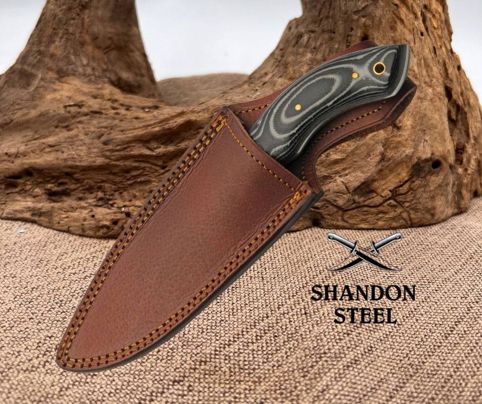 Knife with brown leather sheath on a textured surface, Shandon Steel logo visible