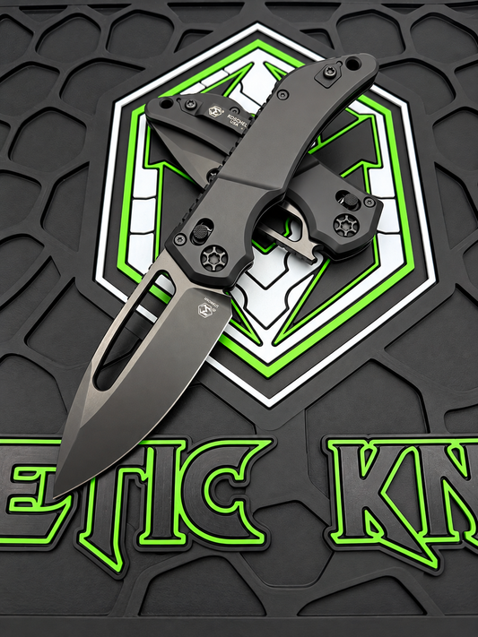 A black tactical folding knife with a matte finish is displayed open on a textured black mat featuring a green and white geometric logo and the partial brand name 'METIC KNA'.