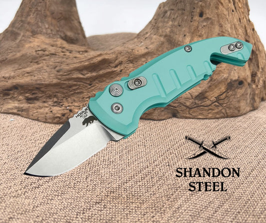 Teal folding knife on a textured surface with 'Shandon Steel' branding.