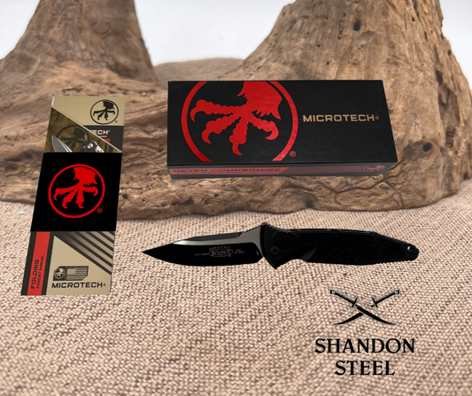 Microtech 160A-1T SOCOM Elite S/E knife with black handle and two-tone black blade, displayed next to its packaging box with red Microtech logo, and 'Shandon Steel' text.