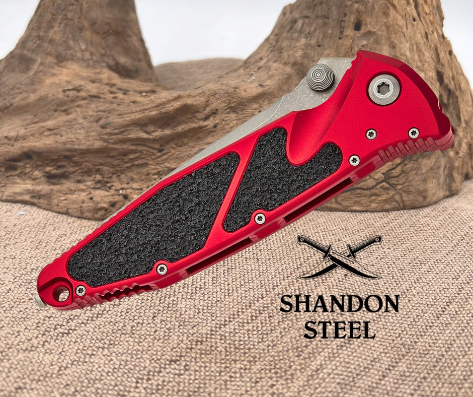 Red folding knife with black grip on a textured surface, featuring the Shandon Steel logo.