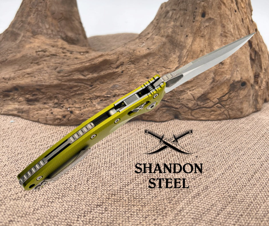 Folding knife with yellow handle and metallic blade on a textured surface, Shandon Steel logo visible.