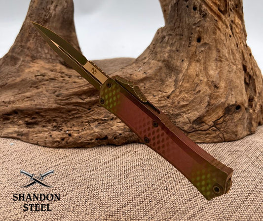 Folding knife with red handle and gold blade on a textured surface, Shandon Steel logo visible