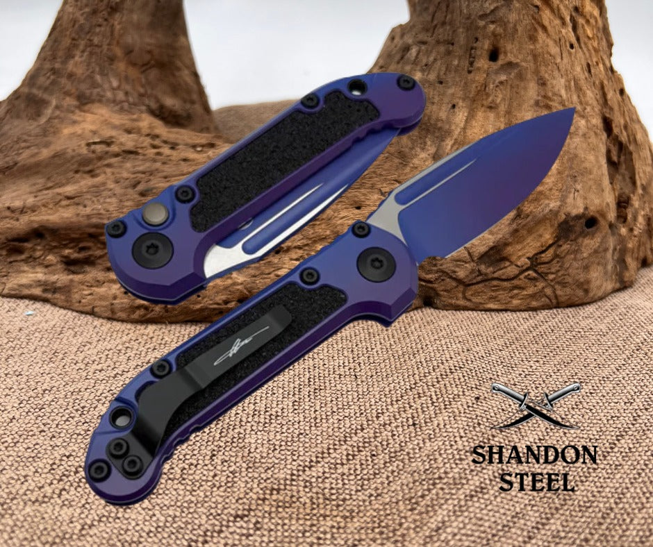 Purple folding knife with black handle on a textured surface, brand 'Shandon Steel' visible