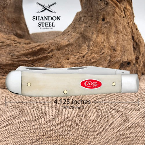 A folding pocket knife shown in side profile on a burlap surface with a piece of driftwood behind it. The knife has a cream-colored handle and silver metal end caps and blades.